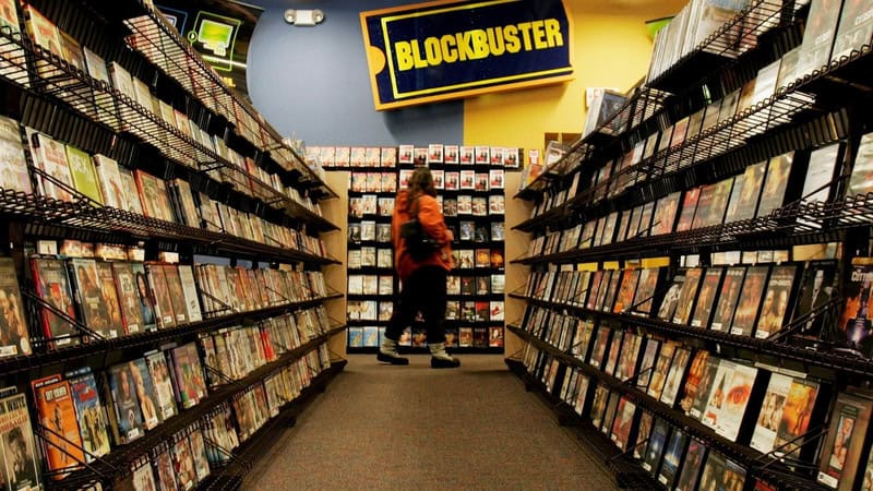A person browsing DVDs in a store with a 'Blockbuster' sign overhead.