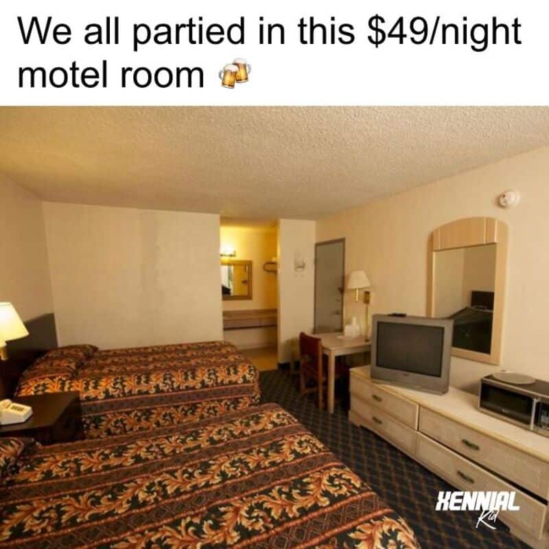 Group of friends in a motel room with two beds, TV, and mirror, celebrating with drinks.