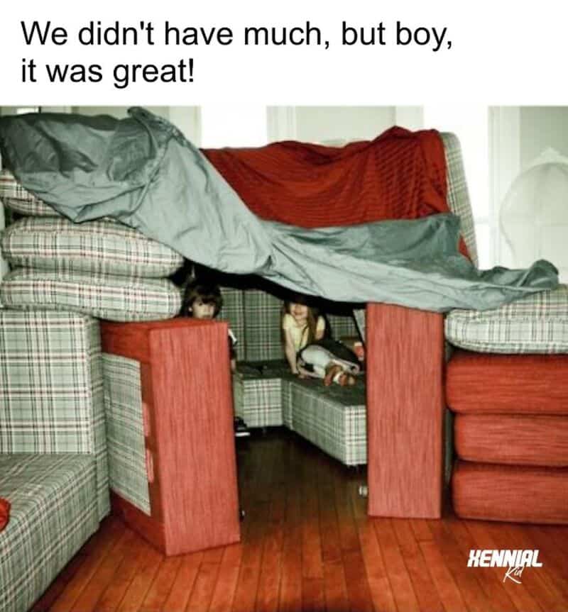 Kids playing under a blanket fort made from furniture and blankets.