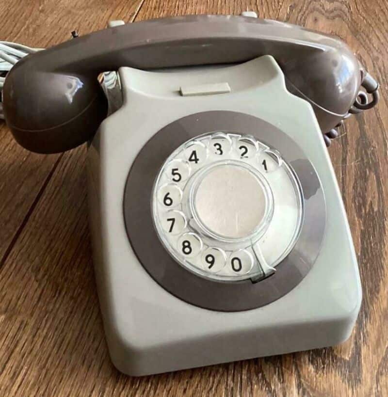 Vintage rotary phone with gray body and black dial on wooden surface.