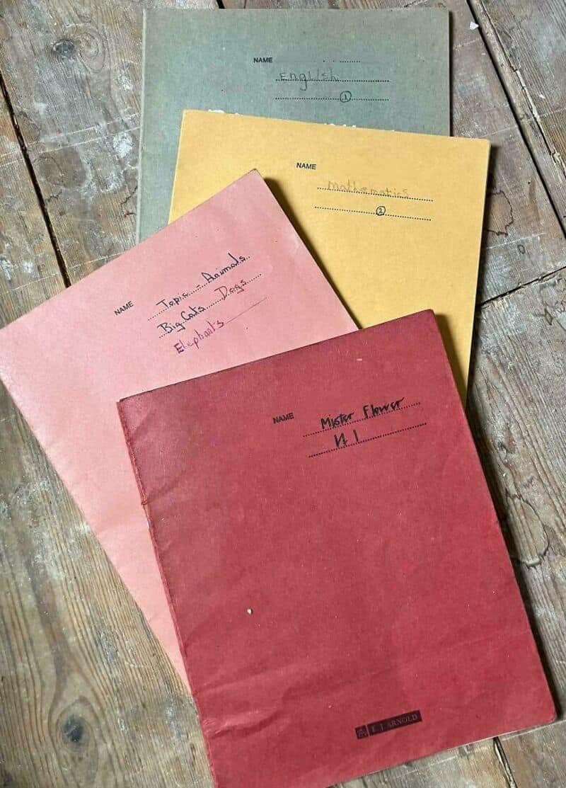 Four vintage school notebooks on a wooden surface, labeled for different subjects.
