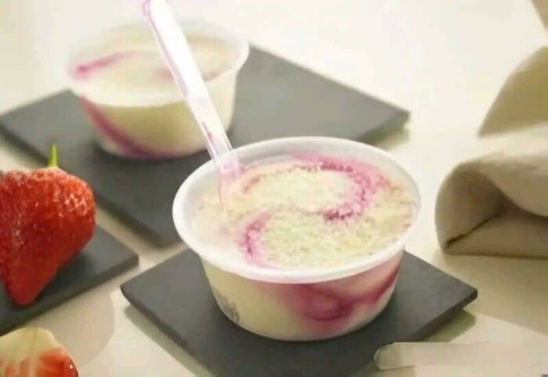 Frozen yogurt with pink swirl in a cup with a spoon, strawberries nearby.