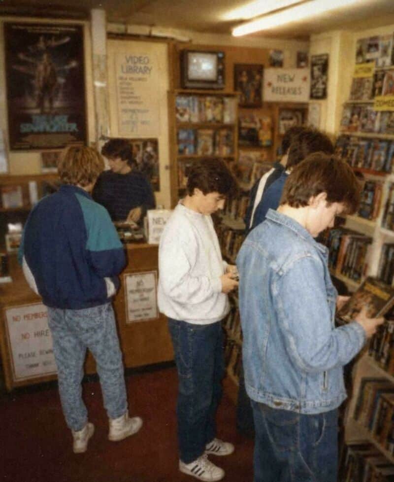 Group of teenagers browsing books in a vintage video store, 1980s style.