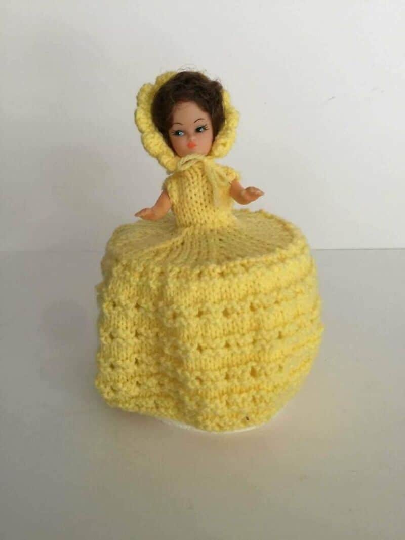 Vintage doll in a yellow knitted dress and bonnet on a white background.