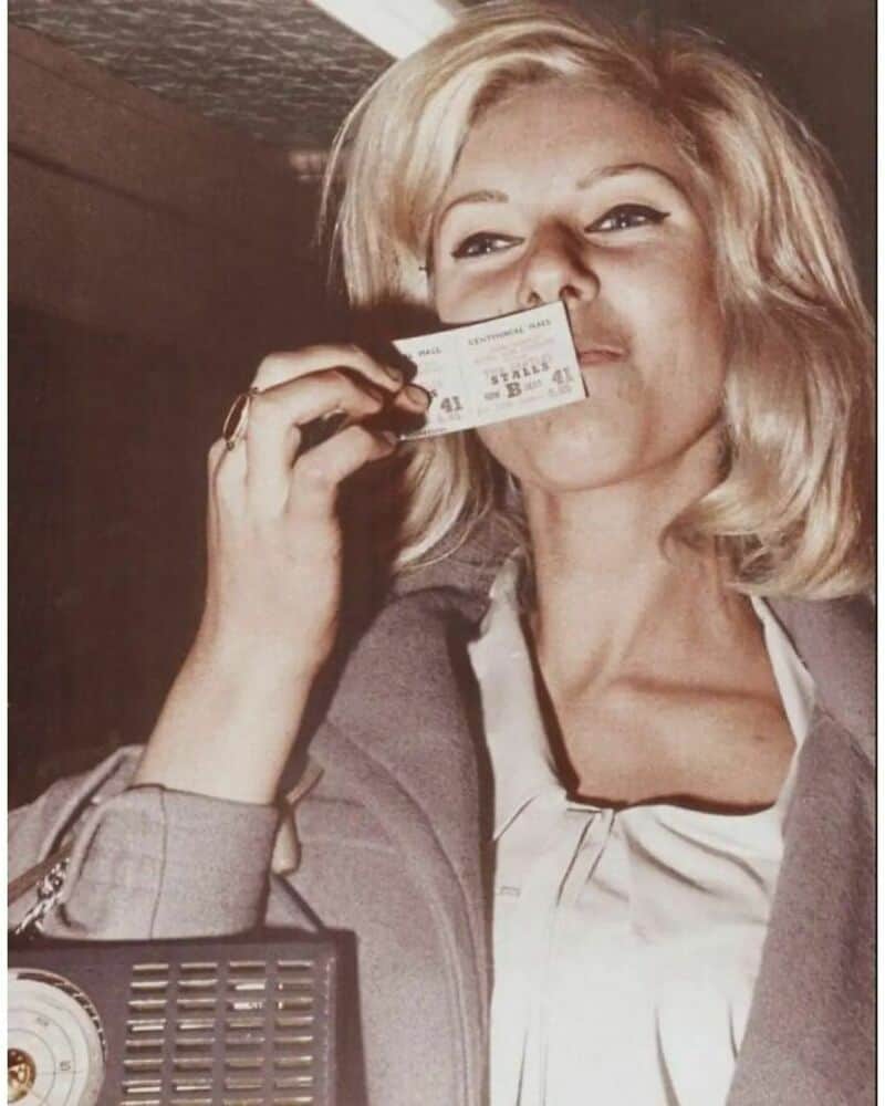 Woman with blonde hair holding a ticket in front of her nose.