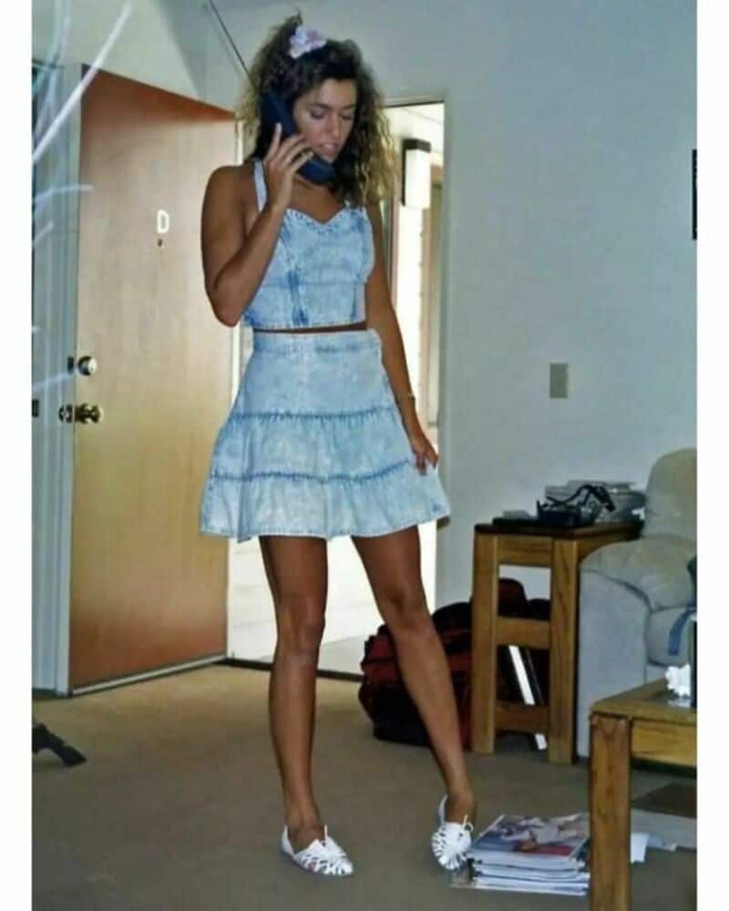 Young woman in a blue dress talking on a phone in a room.