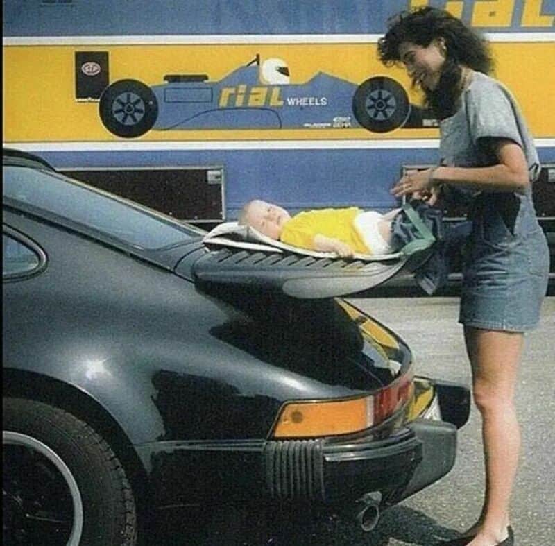 Woman with dark hair and glasses looking at a baby on a changing table in a parking lot.