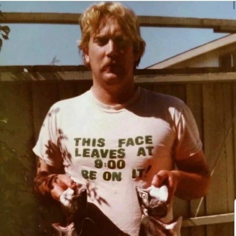 Young man with messy hair wearing a white T-shirt with text, holding two fish.