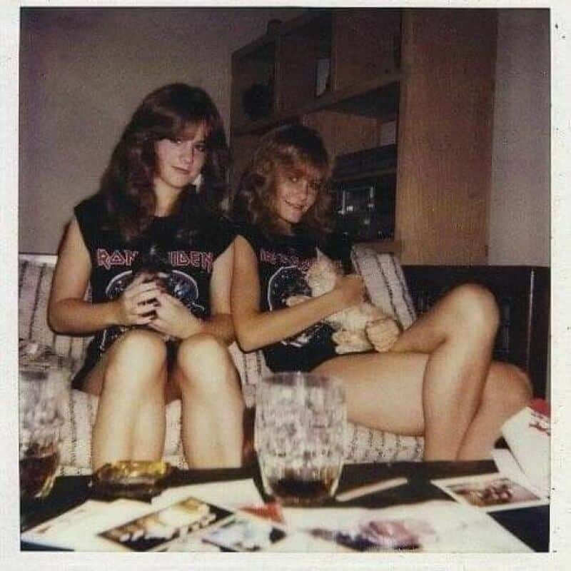 Two young women with long hair in black Iron Maiden t-shirts sitting on a couch.