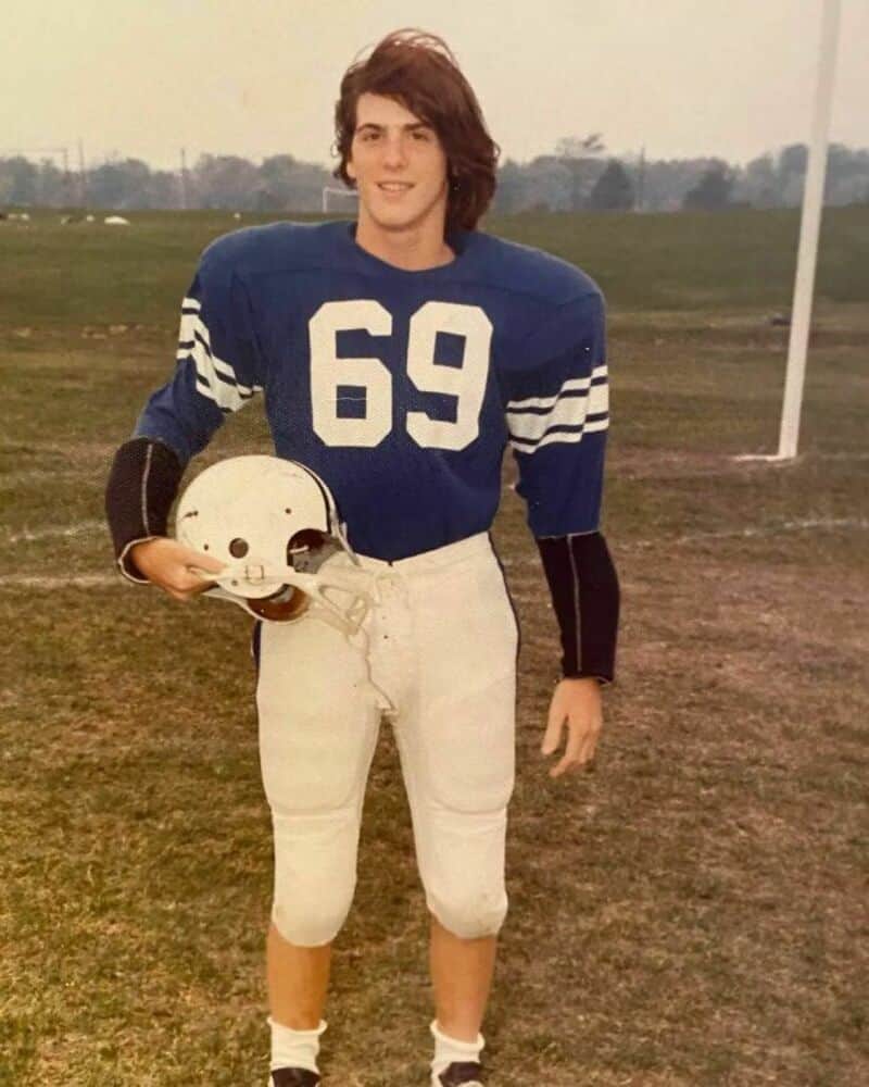 Young football player in blue jersey with number 69, holding helmet, on field.