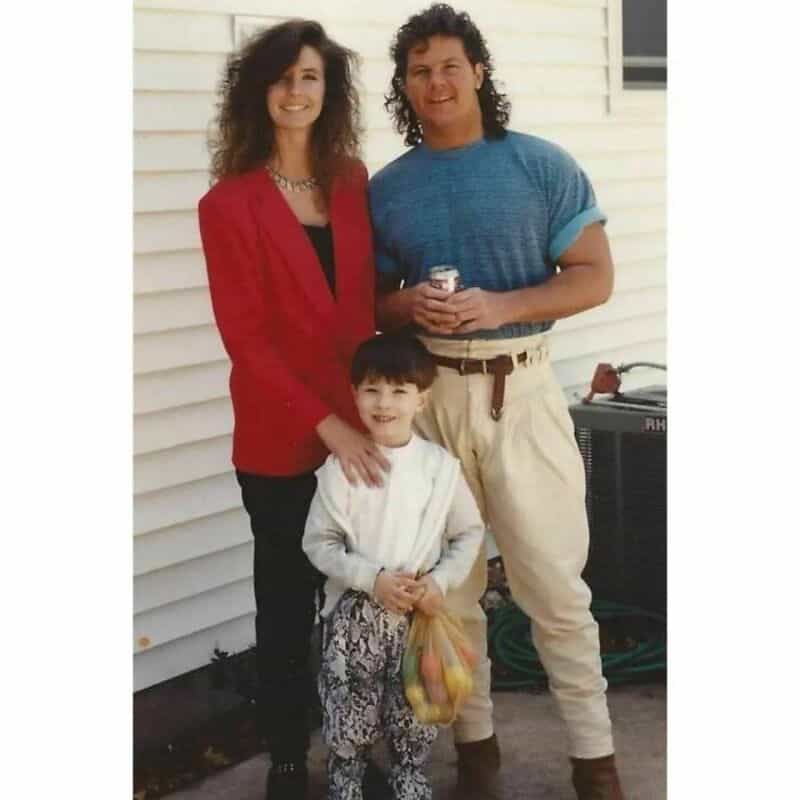 Family photo of two adults and a child standing outside a house.