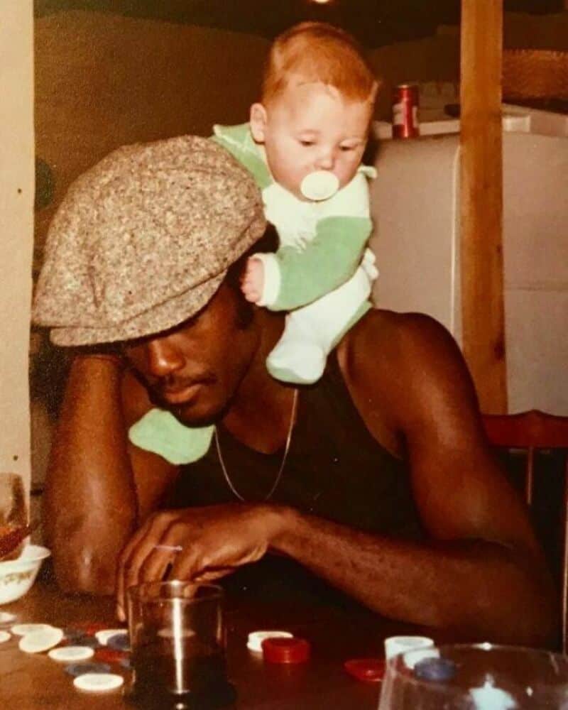 Young man with a baby on his shoulder, wearing a hat, in a cozy indoor setting.