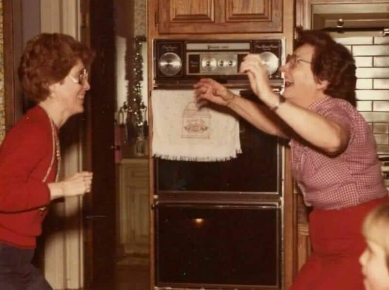 Two women dancing happily in a kitchen with a vintage oven.