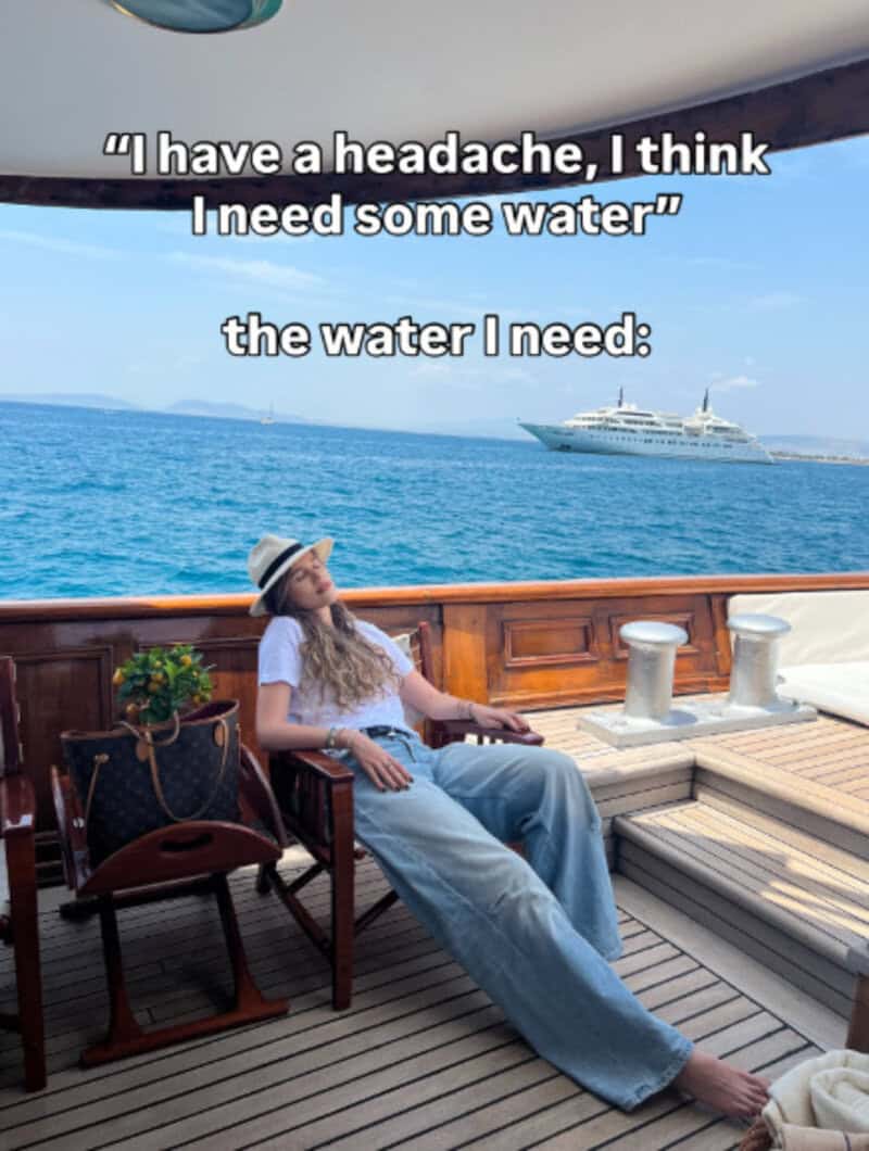 Woman relaxing on a boat deck with water and a yacht in the background.