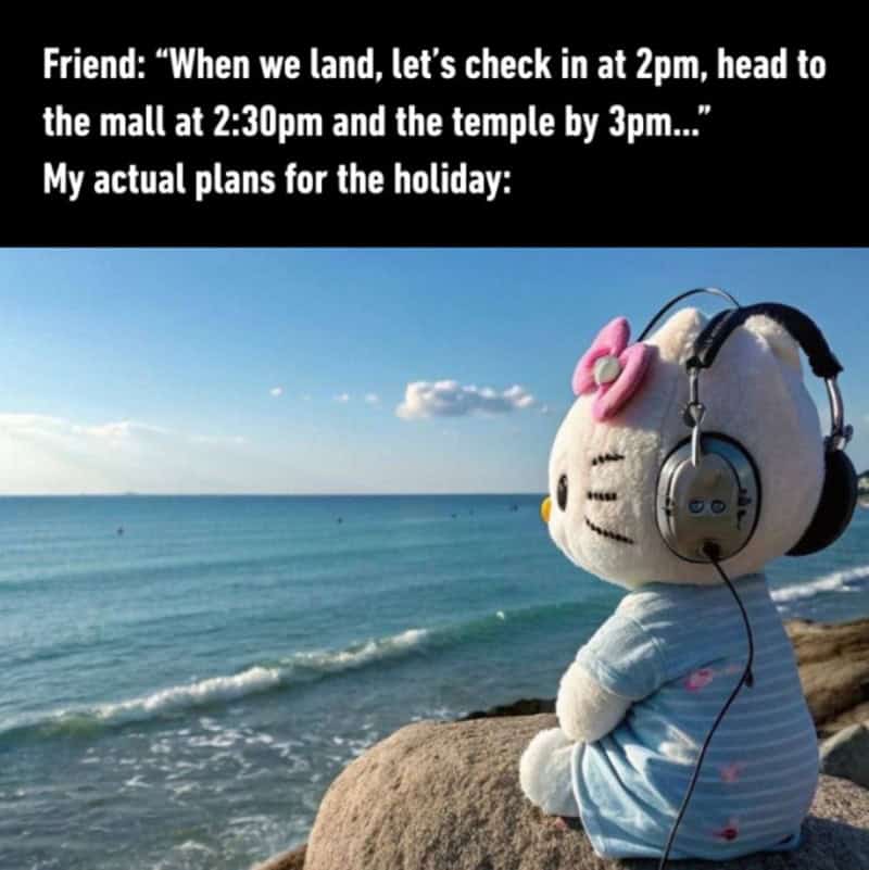 Hello Kitty plush toy with headphones sitting on a rock by the sea.