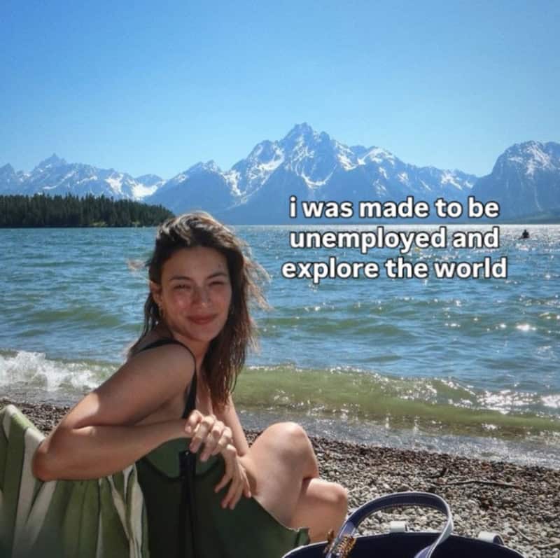 Young woman relaxing by a lake with mountains in the background, smiling.