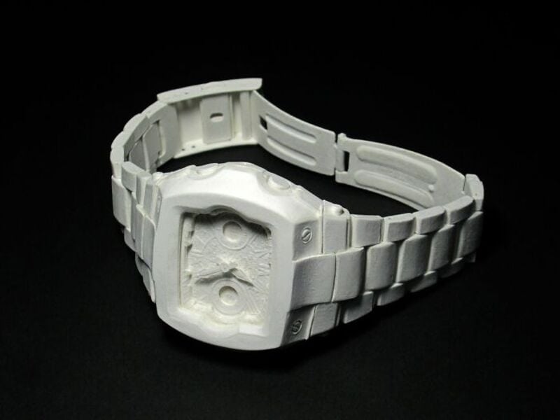 White paper sculpture of a retro electronic watch on black background.