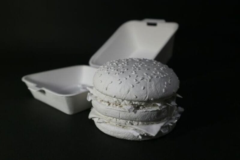 White burger with sesame seed bun and white filling in a white container.