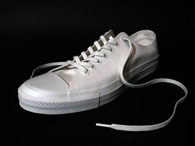 White sneaker with a long shoelace on a black background.