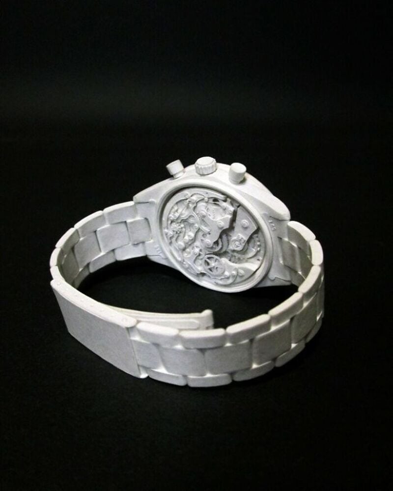 White watch with intricate design on the face, bracelet style band, on black background.