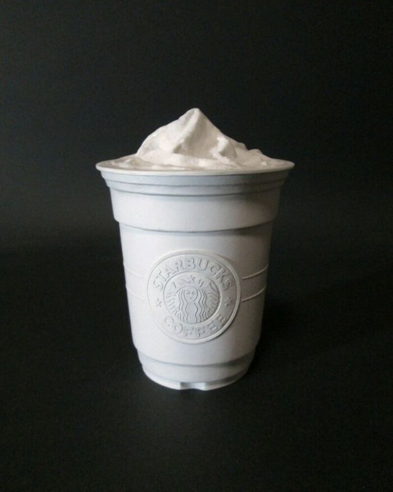White Starbucks cup with whipped cream on top, against a black background.