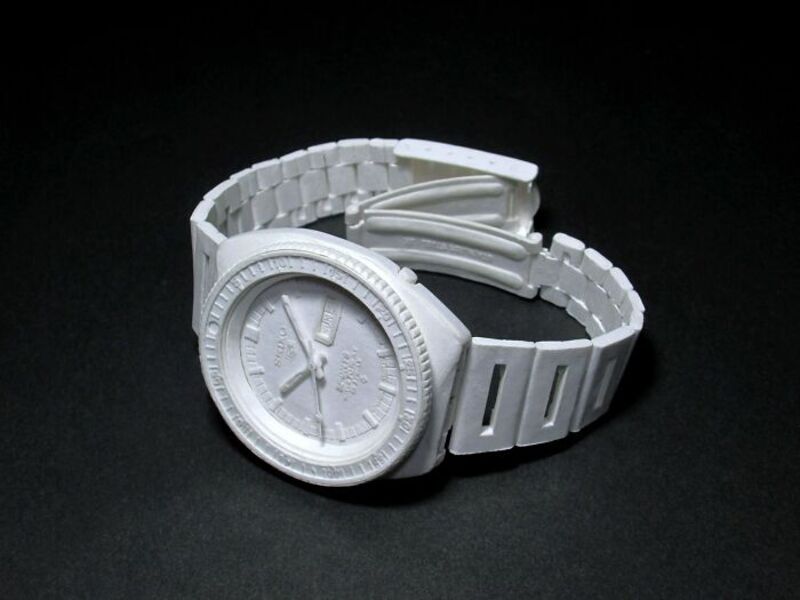 White paper sculpture of a wristwatch with a band, on a black background.