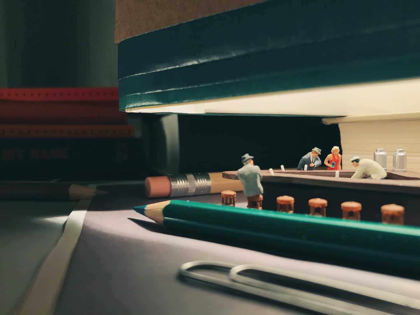 Miniature figures working in a diorama with books and art supplies around.