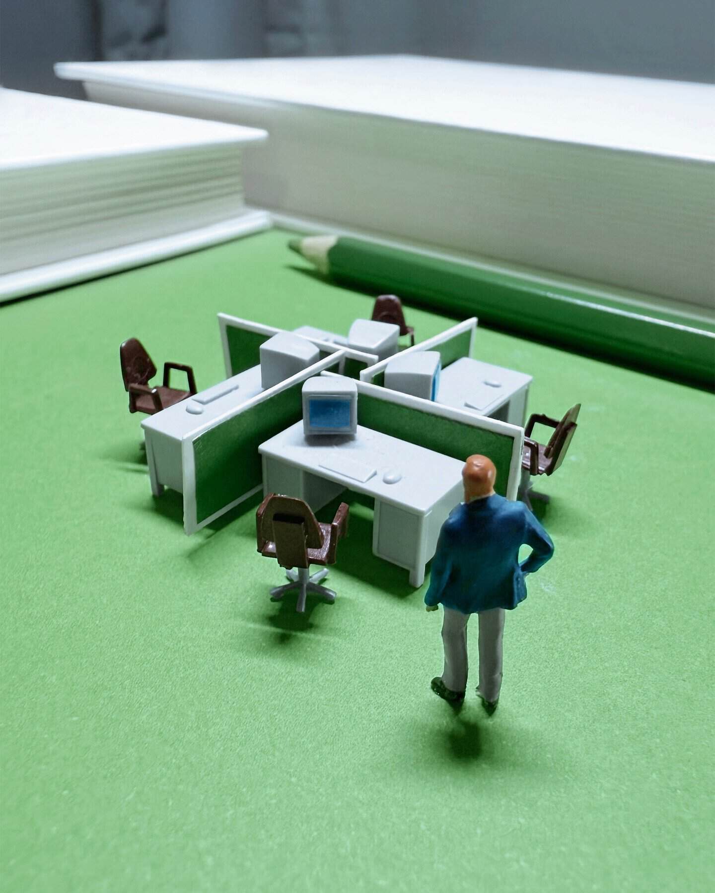 Miniature office scene with tiny desks, chairs, and a figure standing nearby.