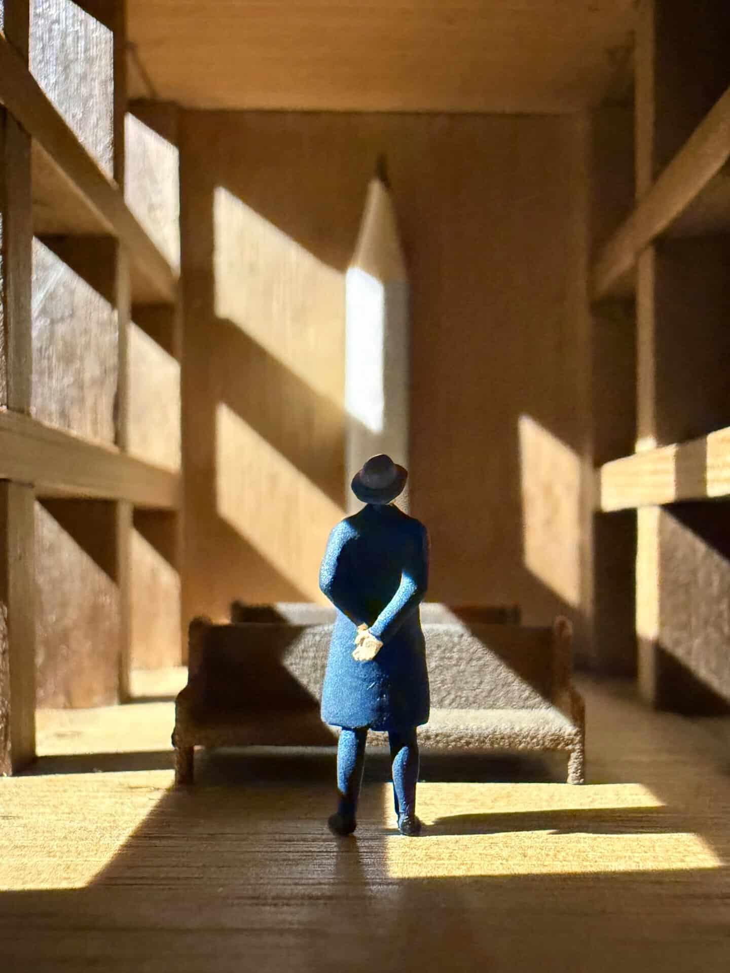 Miniature figure of a woman in a blue coat and hat looking out a window.