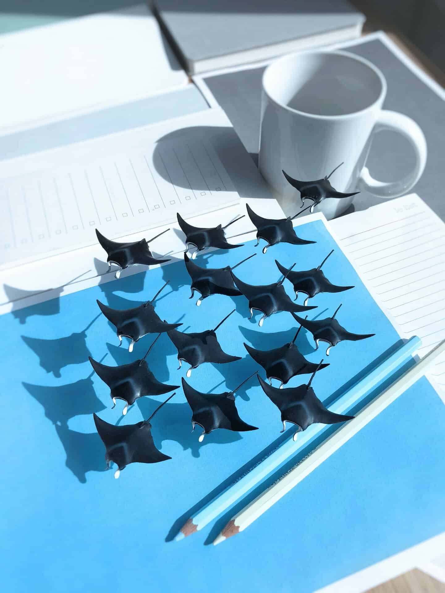 Miniature black cats on blue paper with pencils, a mug, and a notebook.