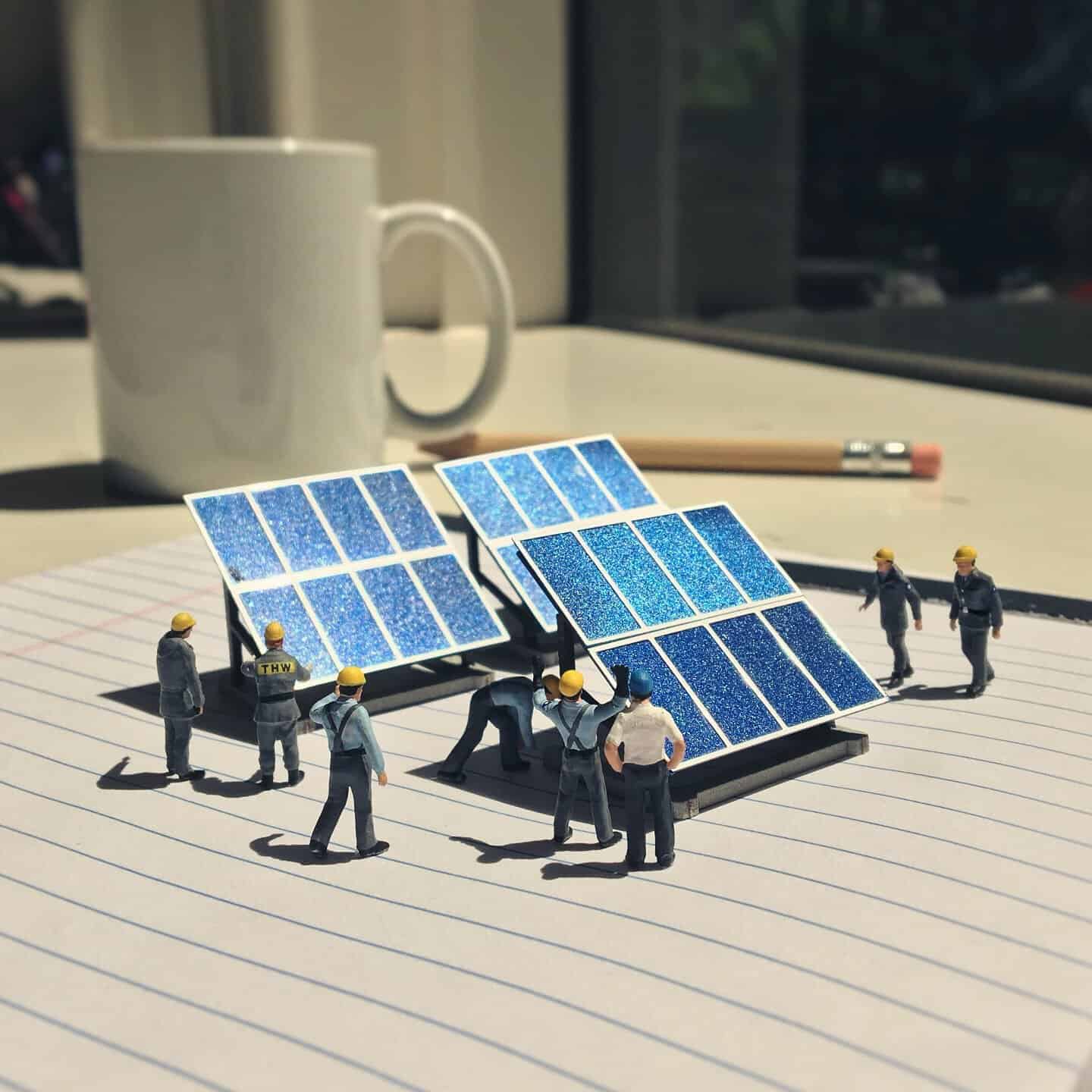 Miniature figures working on solar panels on a notebook with a mug and pencil in background.