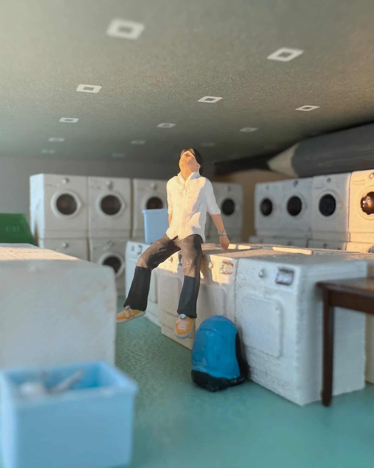 Miniature figure sitting on a laundry machine in a laundry room diorama.