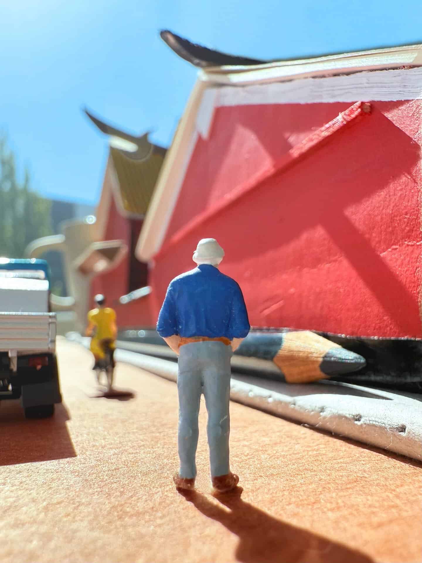 Miniature man figure with a blue jacket and gray pants standing near a large red book.