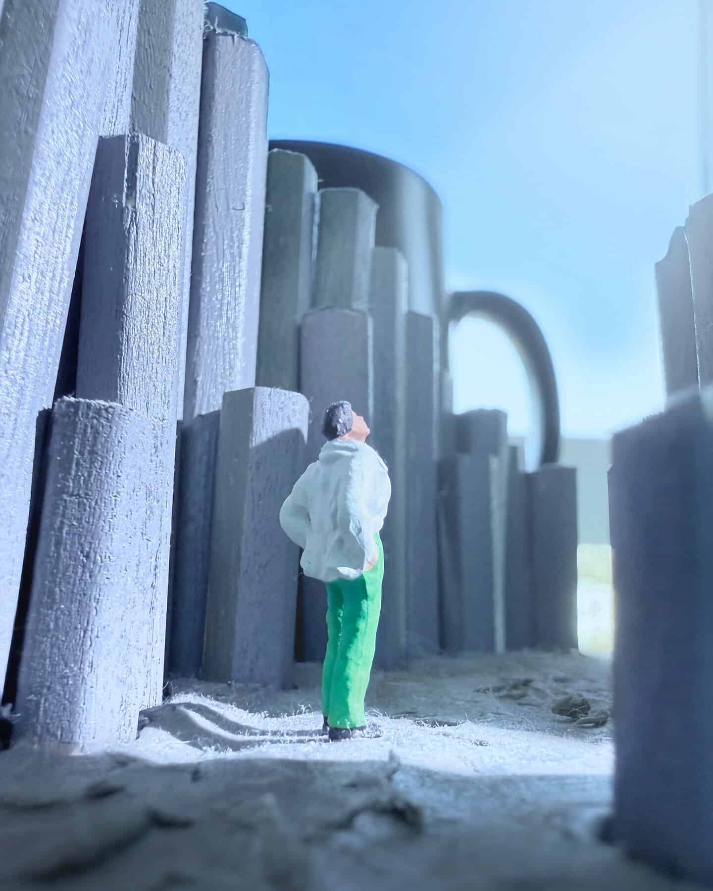 Miniature figure of a man in white coat and green pants among tall structures.