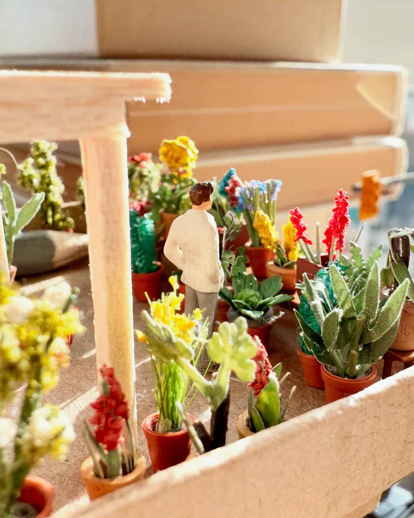 Miniature man figure among potted plants and succulents in a diorama scene.