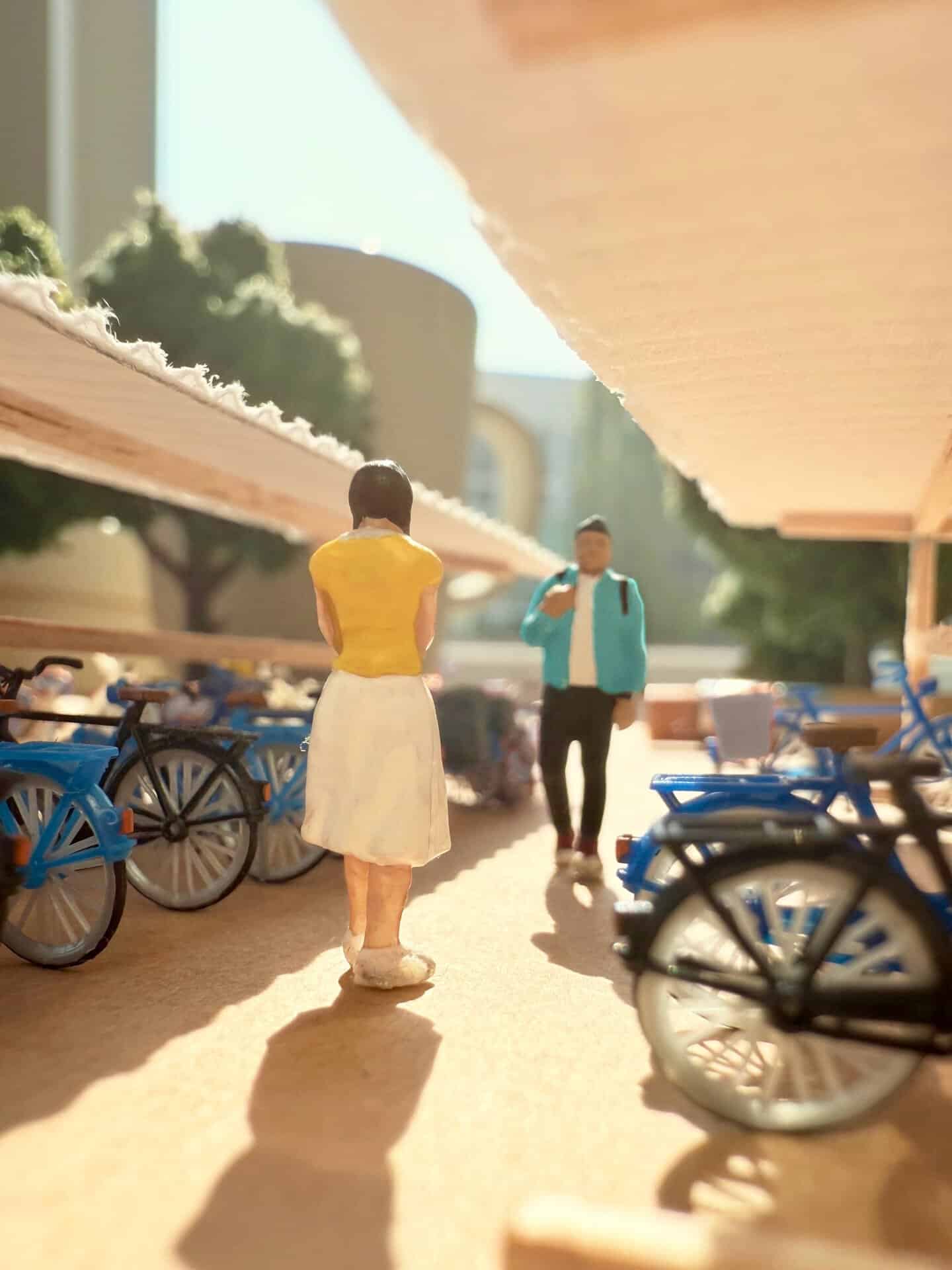 Miniature figures of a woman and a man in a park with bicycles and trees.