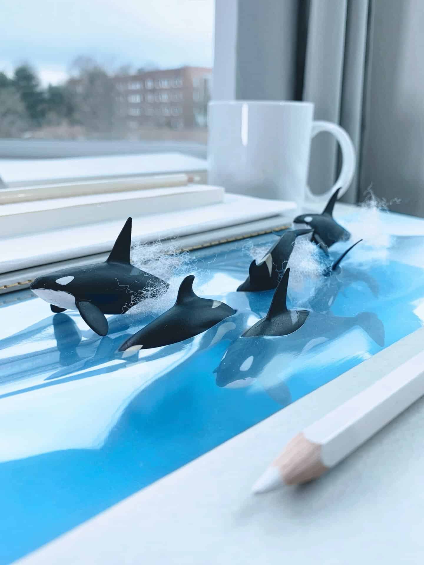Miniature orca figures swimming in a blue water scene on a windowsill.