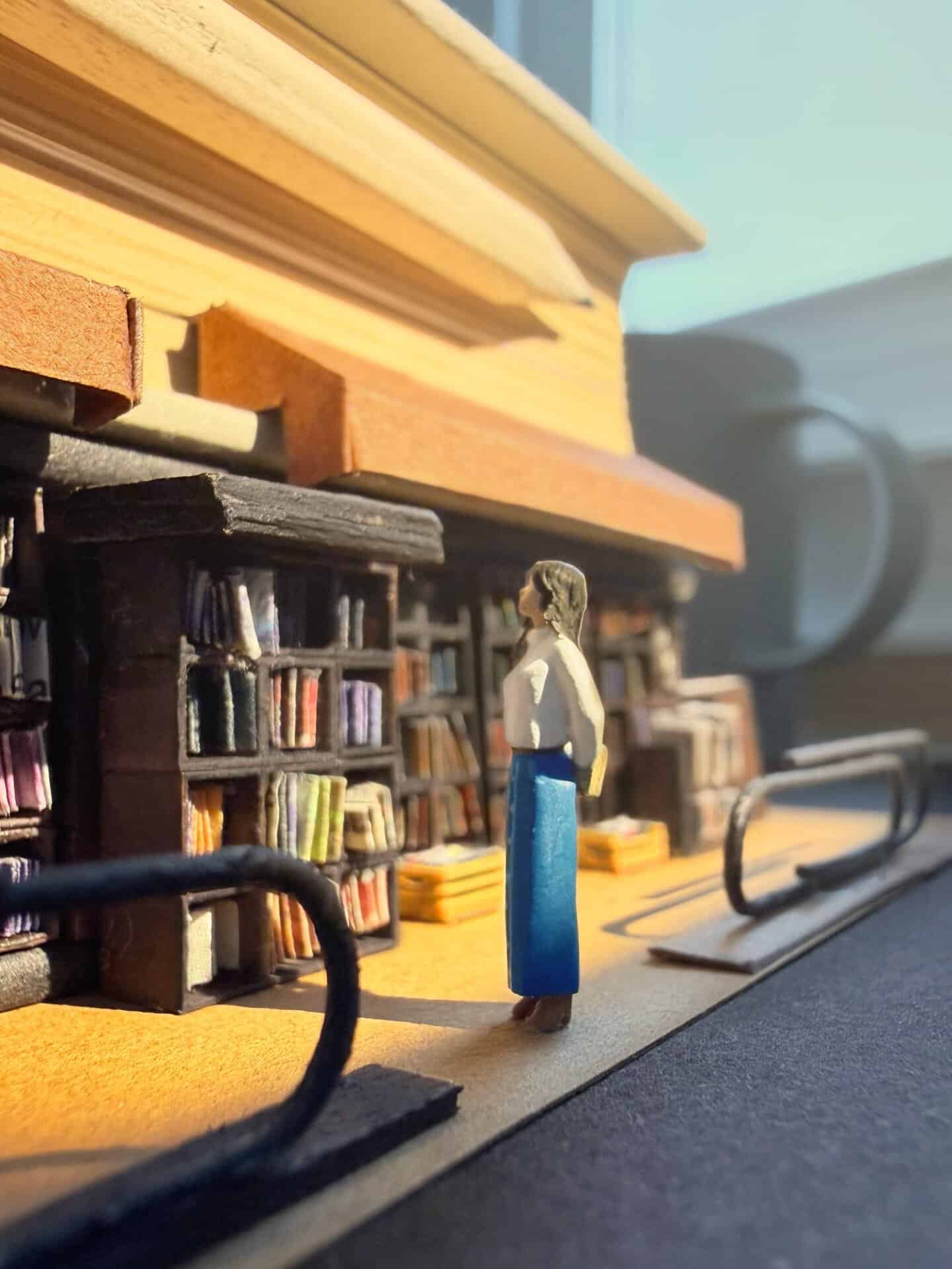 Miniature woman figure standing in front of a bookshelf with books and objects.