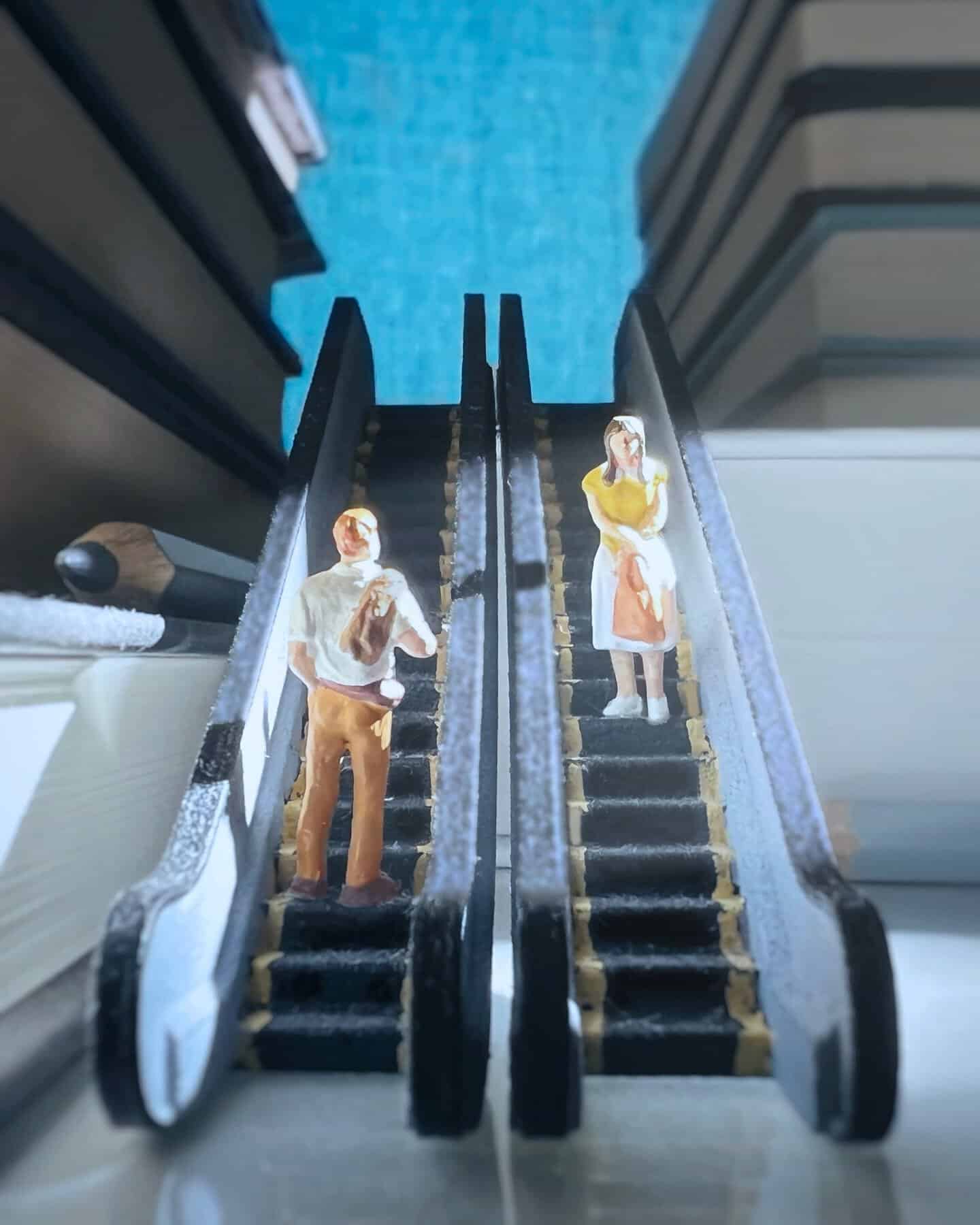 Miniature figures on escalators with a blue background, resembling a real scene.