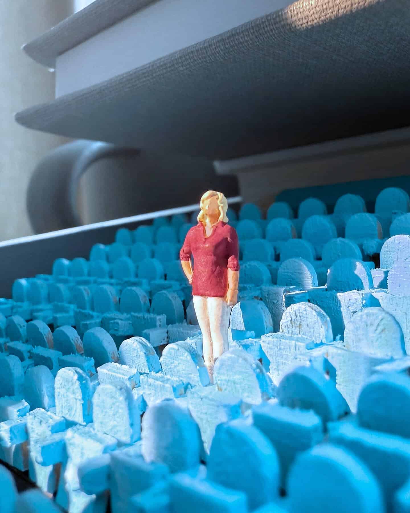 Miniature woman figure standing among blue foam tombstones in a diorama scene.