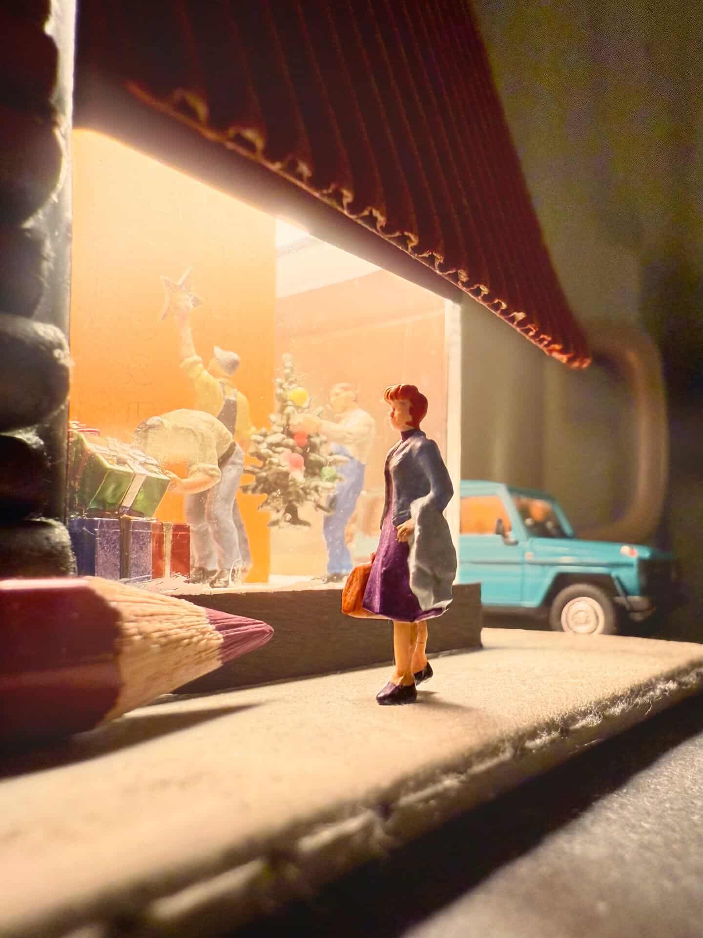 Miniature woman figure looking out a window with a toy car outside.