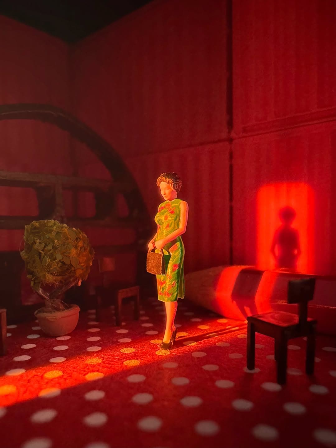 Miniature woman figure with a handbag in a red-lit room with furniture and a potted plant.
