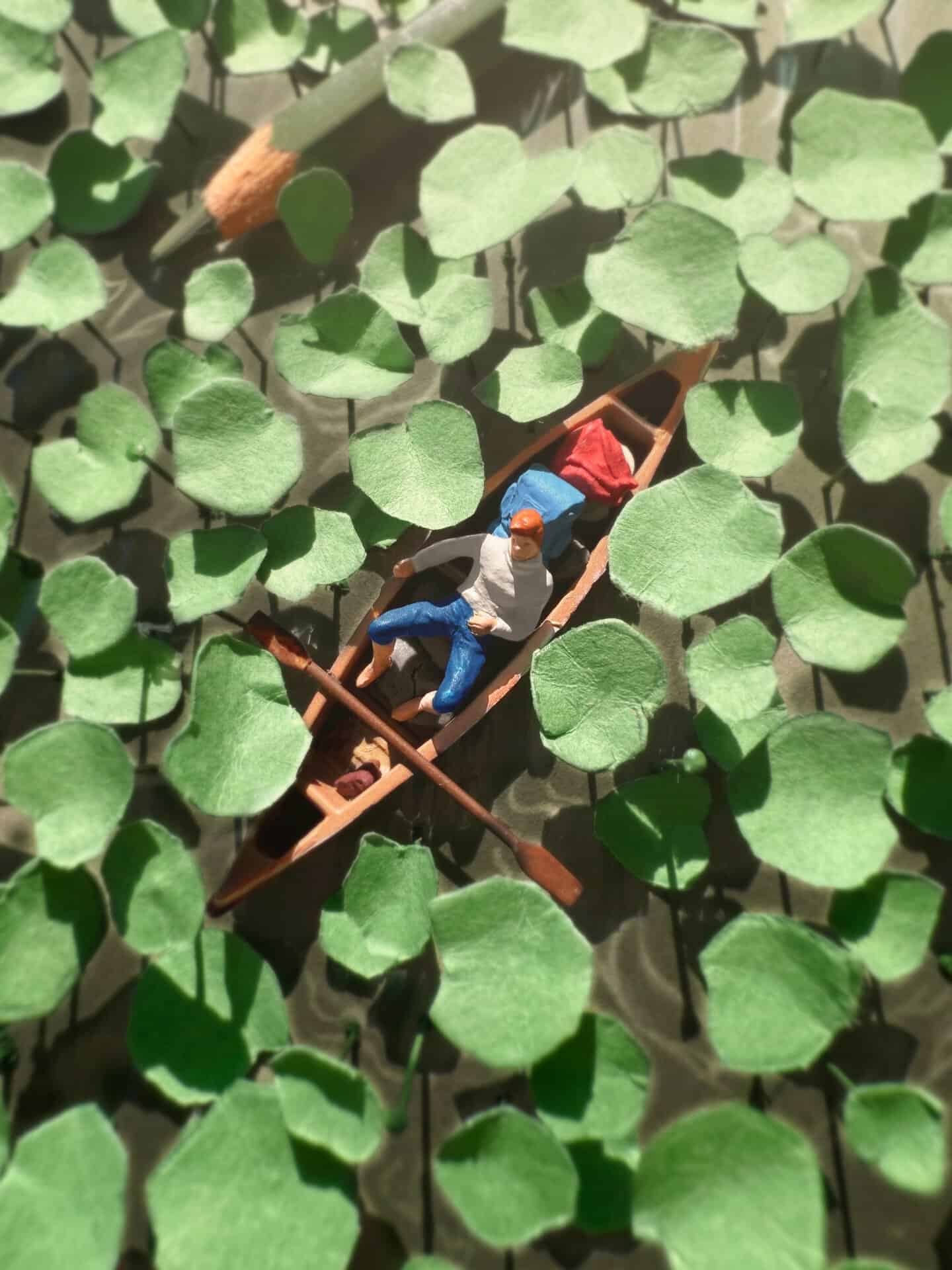 Miniature figures in a boat among green leaves, creating a diorama scene.