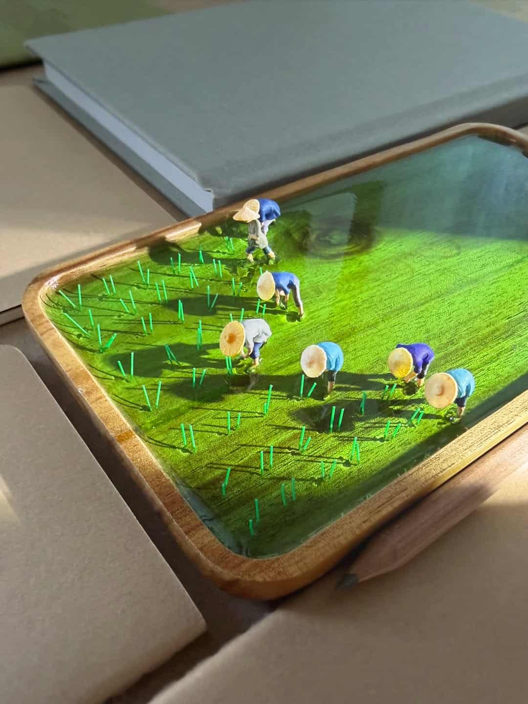 Miniature farmers and sheep on a green diorama landscape with water and grass.