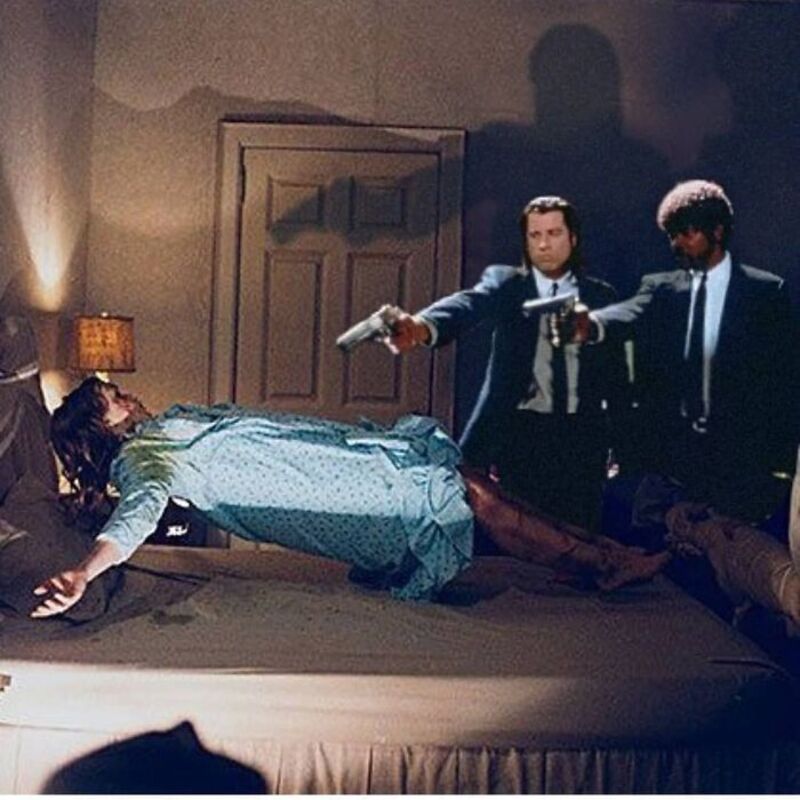 Two men point guns at a woman lying on a bed in a dimly lit room.