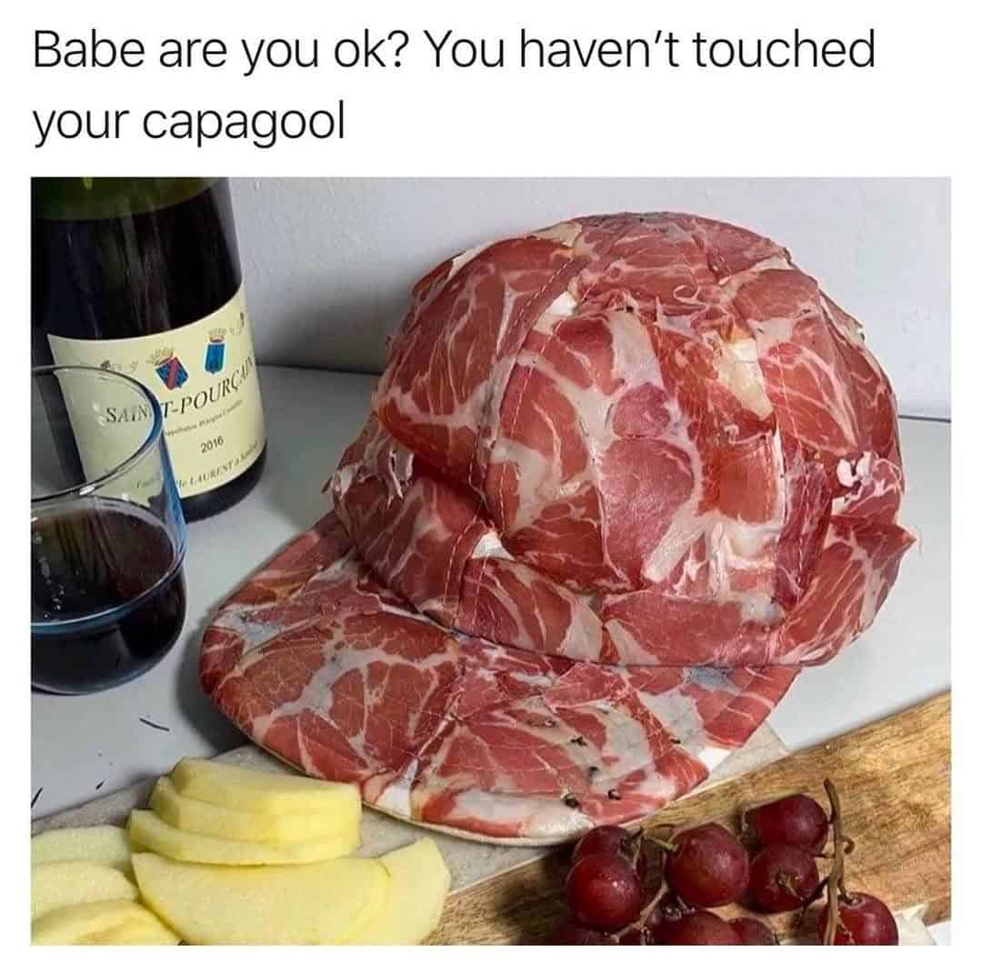 A hat made of sliced ham with grapes, cheese, wine, and a bottle in the background.