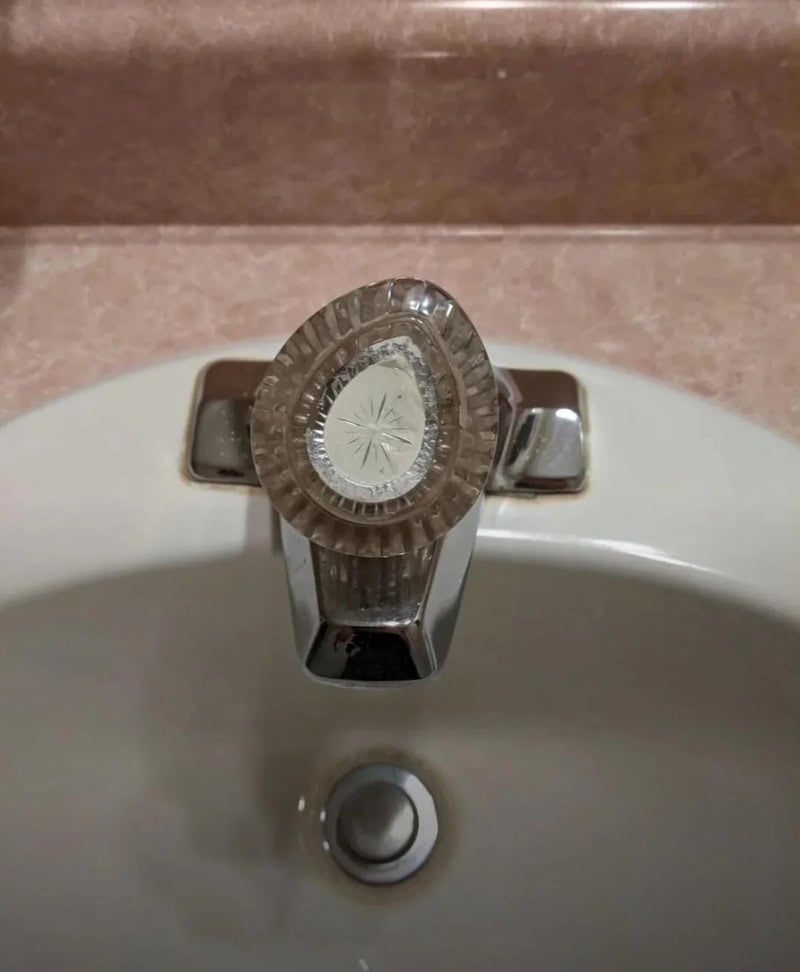 Close-up of a vintage faucet on a bathroom sink with a pinkish wall background.