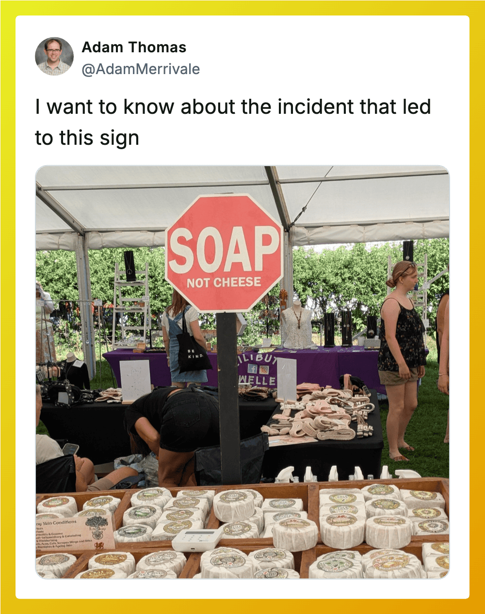 Sign says 'SOAP NOT CHEESE' at outdoor event with tables of soap products.