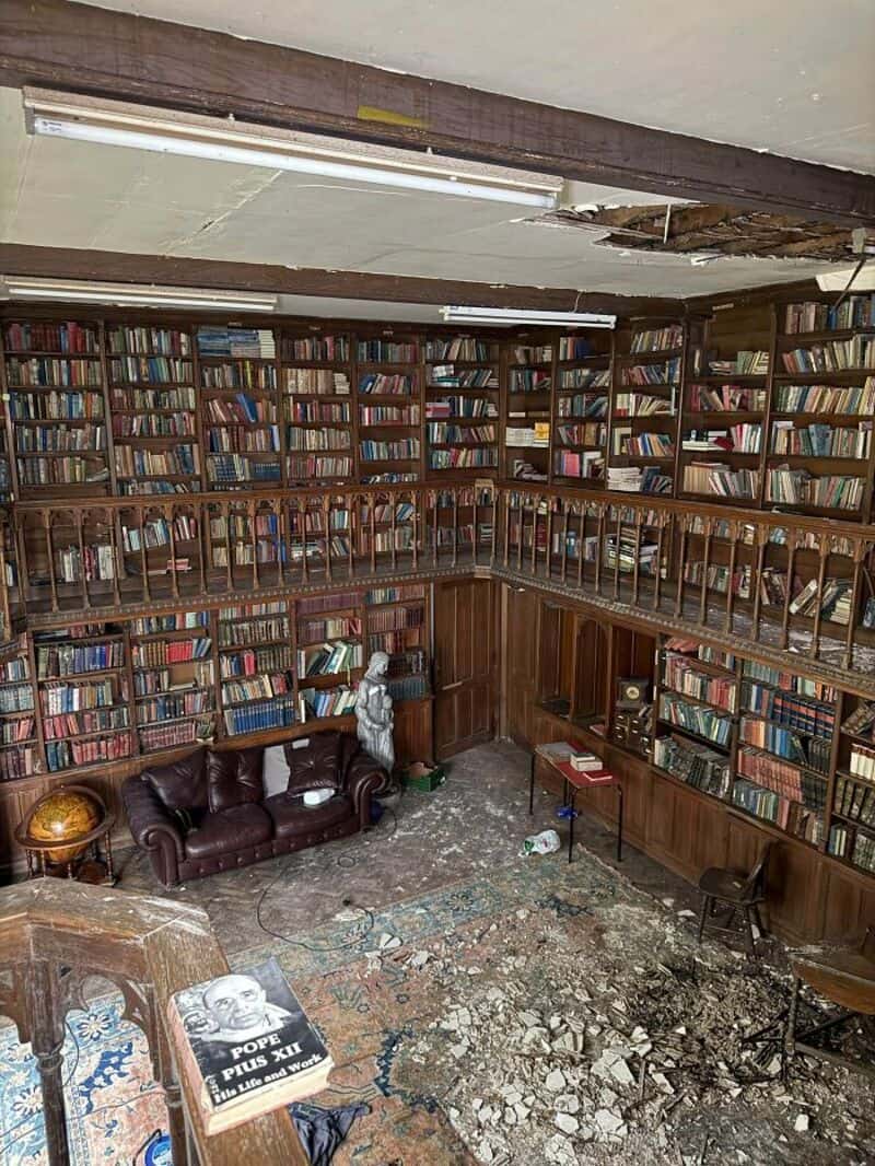 Abandoned library with damaged floor and old books on shelves.