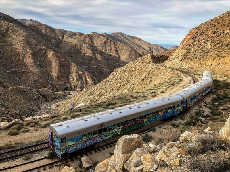 Graffiti-covered train traveling through rugged desert mountains.